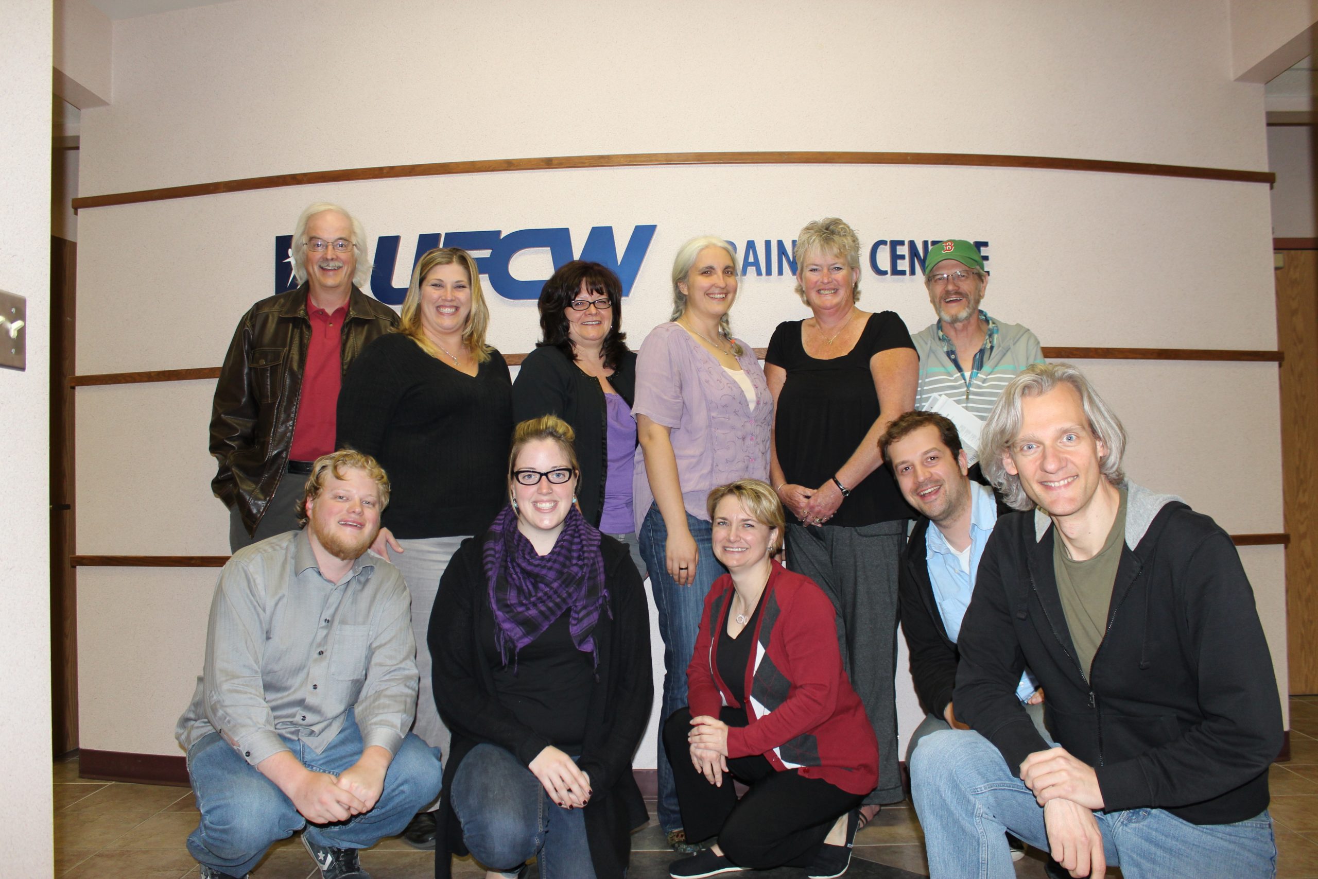 UFCW Local 832 Workshop Group photo at the UFCW training Centre in 2012. 11 people, some crouched down in front of UFCW training centre sign and logo.