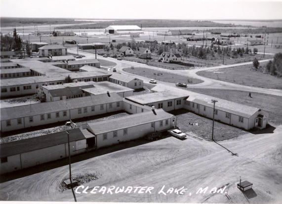 Black and white photo of Clearwater Lake Sanitorium: multiple long one story buildings and a dirt parking lot.
