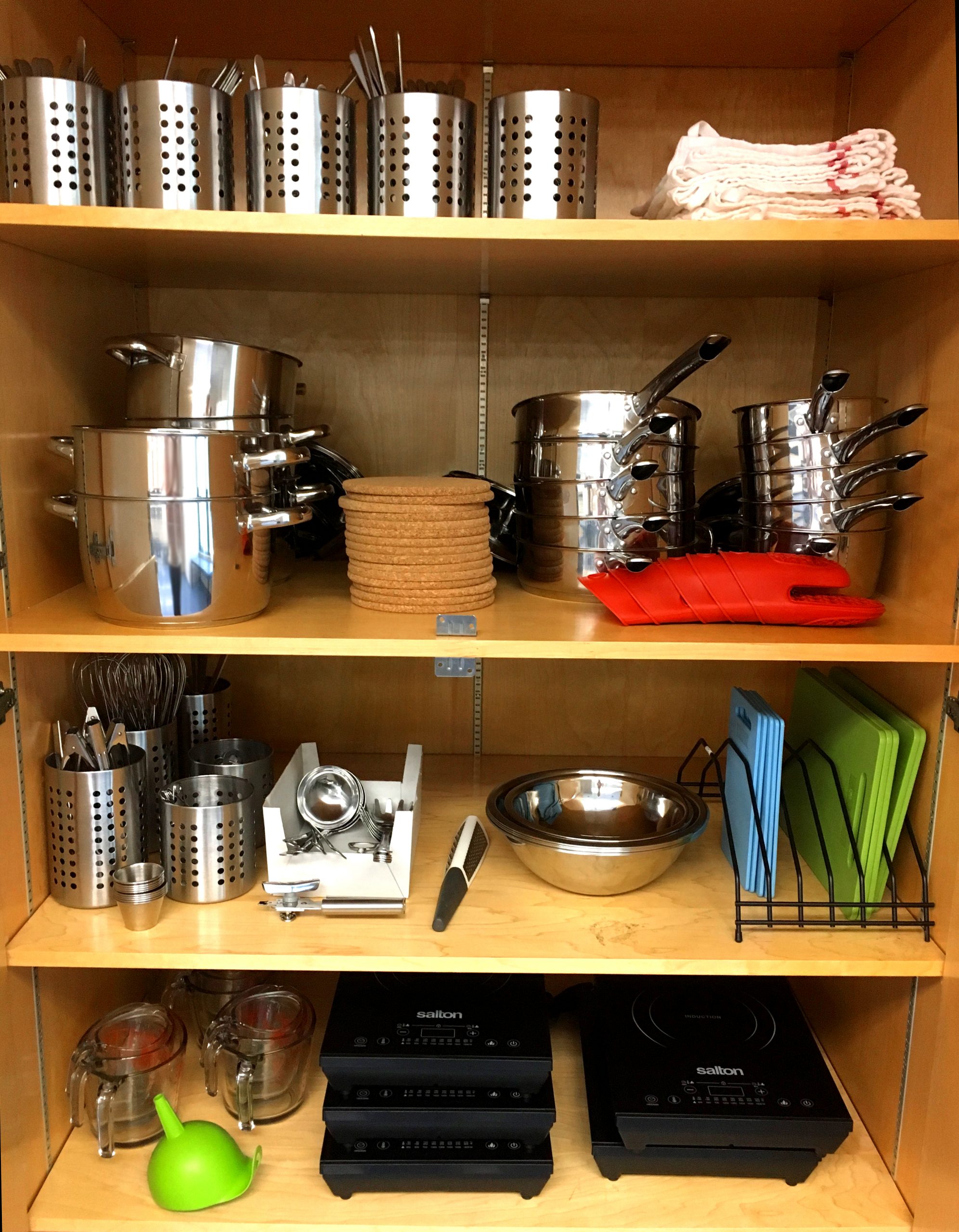 Four shelves of various cookware: pots, pans, cutlery, cutting boards, bowls, hotplates.