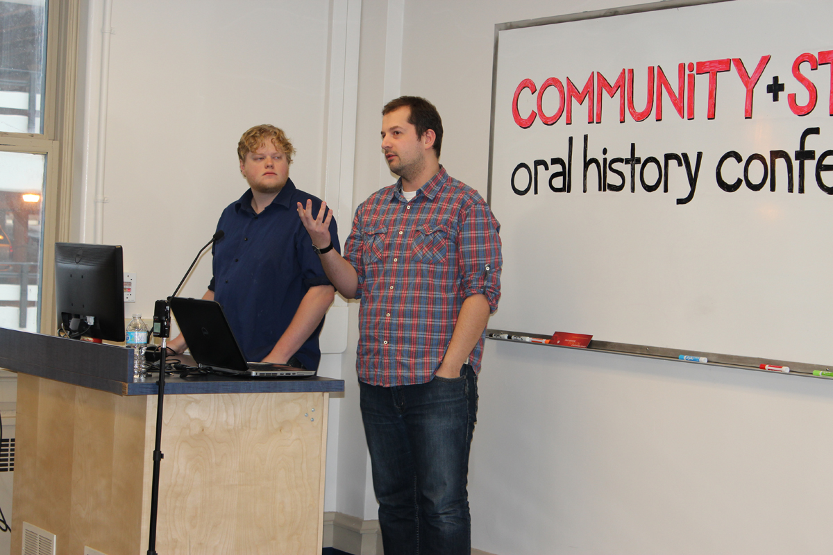 Photo of Kent Davies and Scott Price speaking at podium, whiteboard background with cutoff text: Community + oral history conf