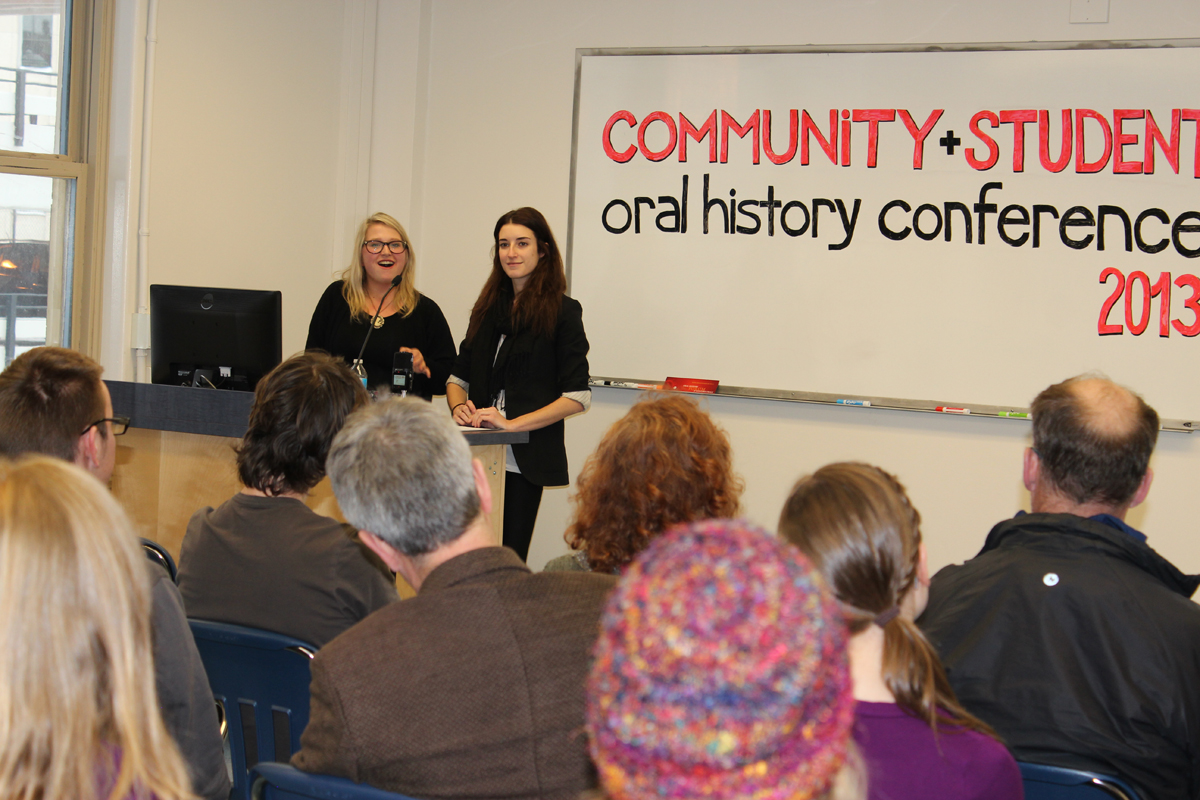 Photo of Haley Caldwell and Lauren Finkle speaking at podium with crowd watching, whiteboard background with text: Community + Student oral history conference 2013