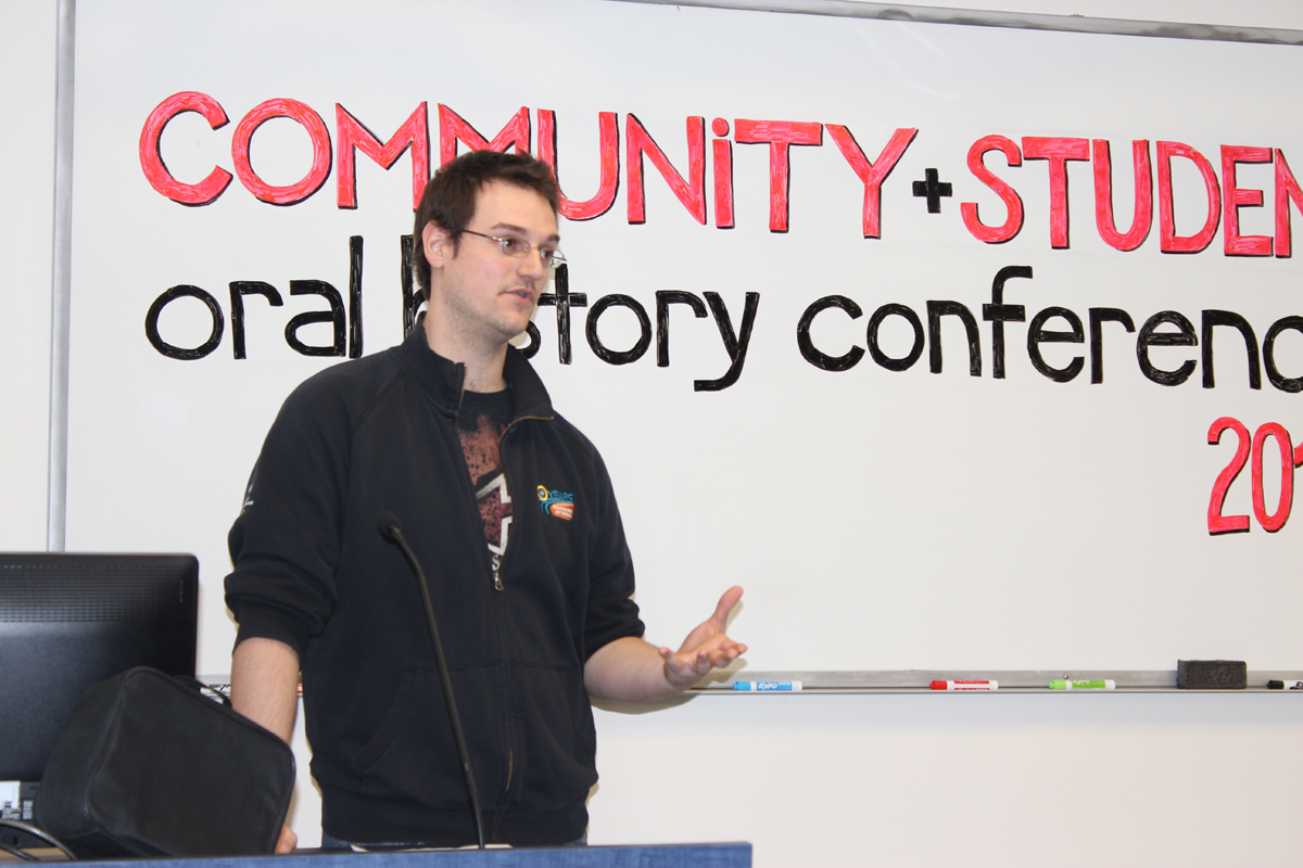 Photo of Matt Tereault speaking at podium, whiteboard background with text: Community + Student oral history conference 2013