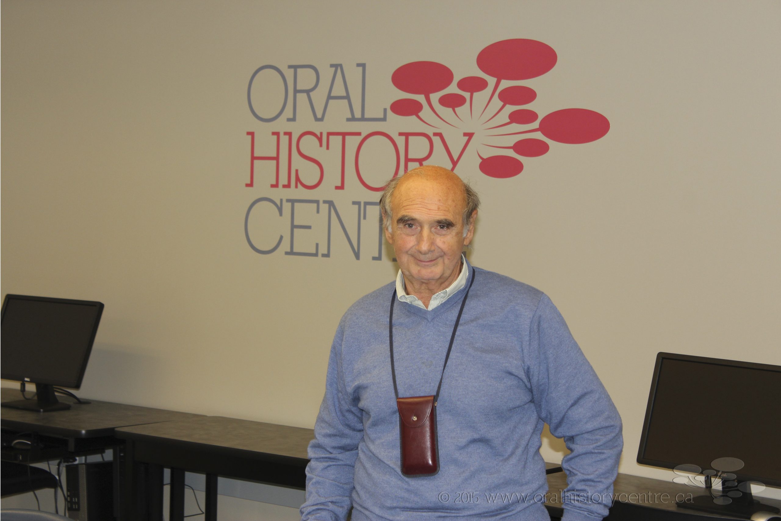 Photo of Dr. Alessandro Portelli in front of a beige wall background with Oral History Centre logo.