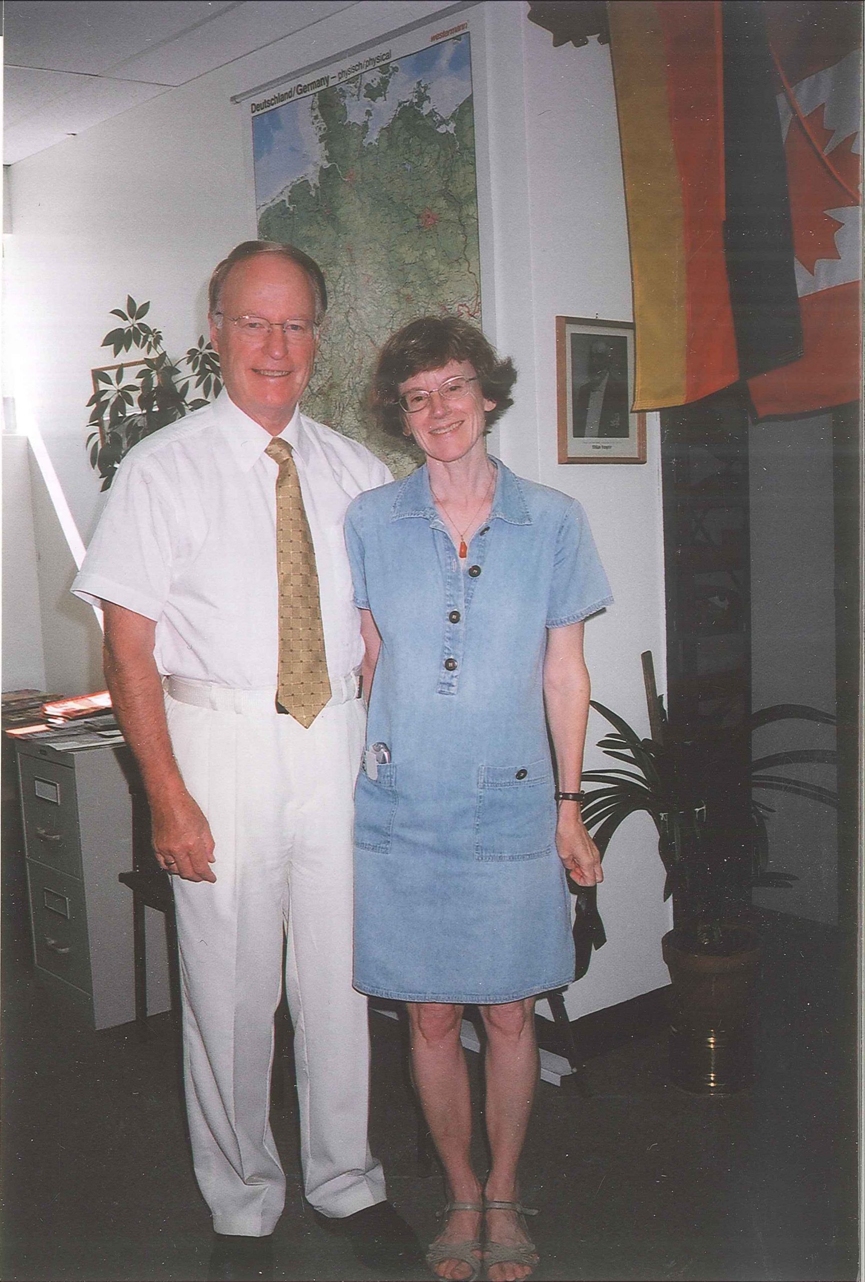 Deborah and Gerry Spindler standing inside the German Honorary Consul in Winnipeg Manitoba. In the background is a map of Germany, and German and Canadian flags.