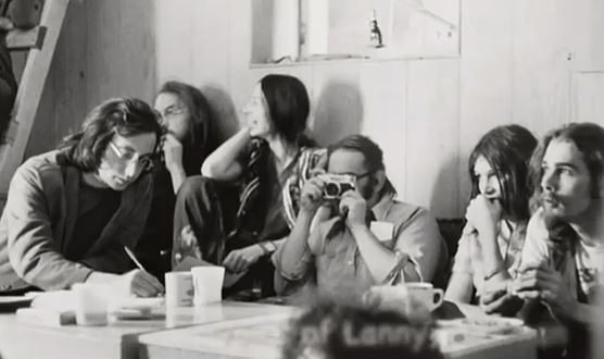 Group Black and white photograph of six members of the Vancouver Mental Patients Association. Coffee cups on a table. One person is laughing, one person is taking a photo, another is writing.