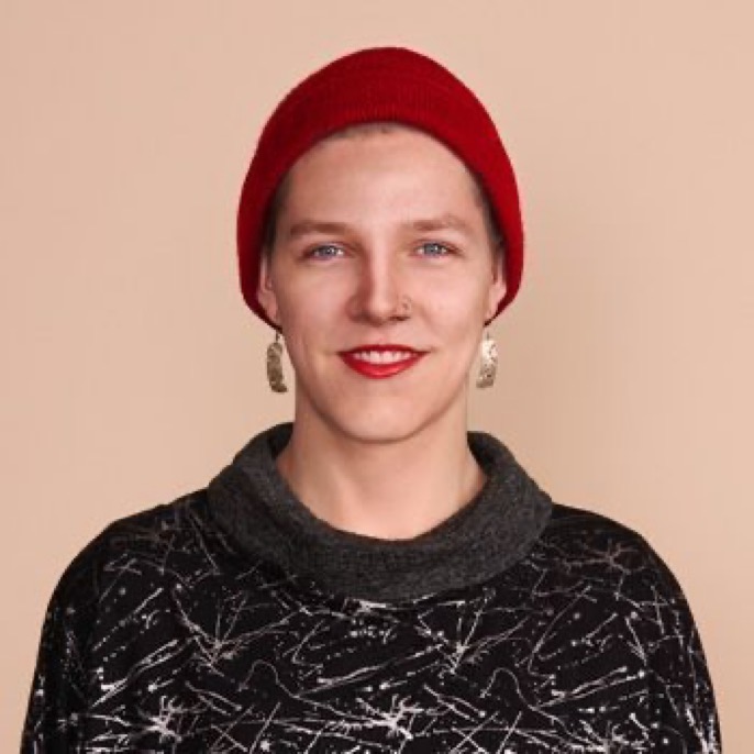 Misha Falk poses for photo in a red cap, black sweater; tan background